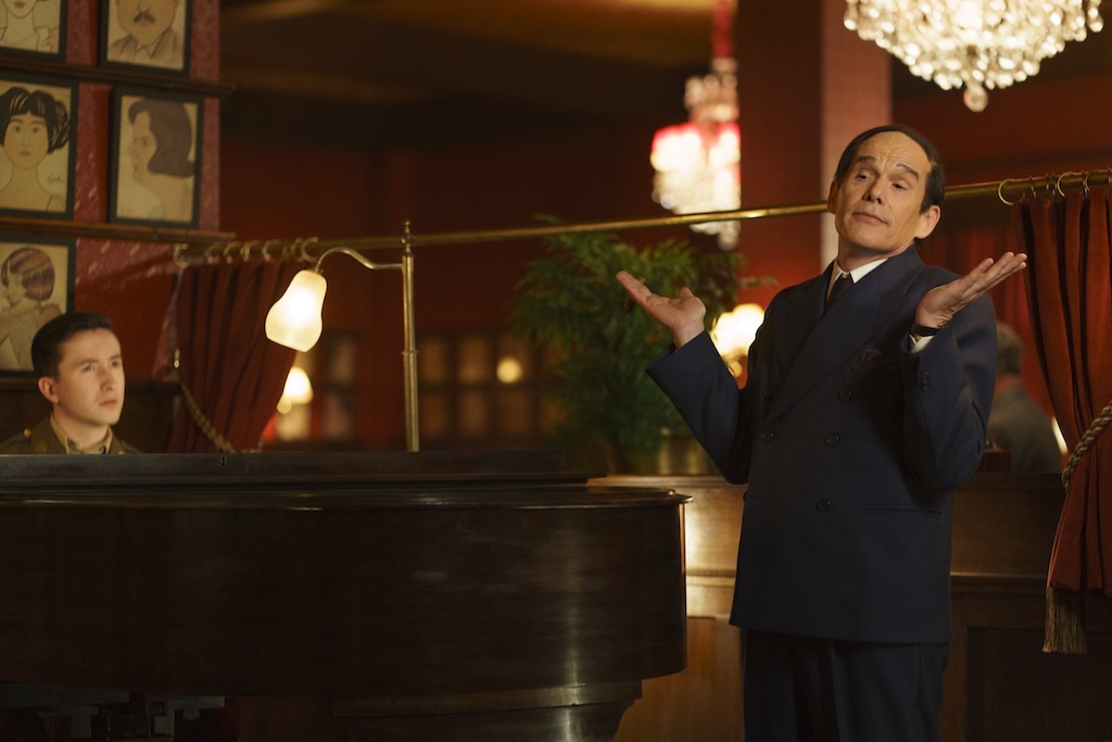 still from Blue Moon - an elfin Ethan Hawke throws his hands up while a young soldier plays the piano in a fancy 40s bar